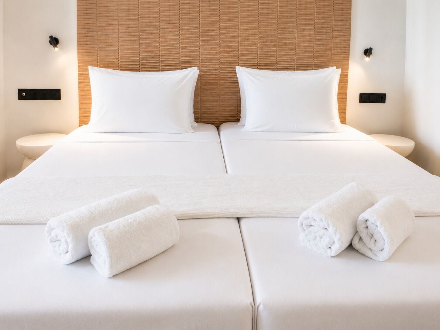 Una cama doble con sábanas y almohadas blancas, dos mesitas de noche y un cabecero con un diseño texturizado.