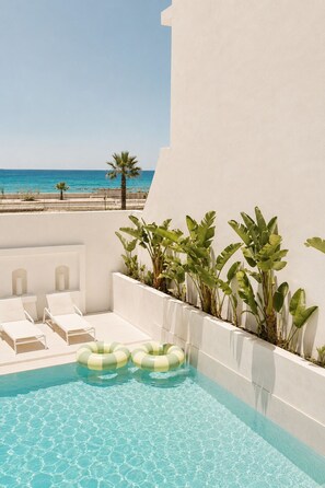 A pool area with clear blue water, white lounge chairs, and tropical plants. - Melitti Lucent (Rethymno)