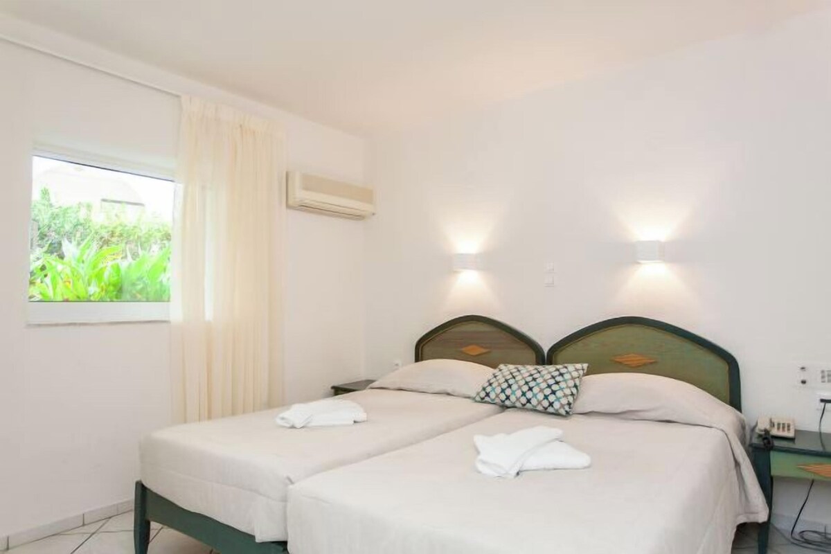 Habitación de hotel con dos camas, una ventana con cortinas, un equipo de aire acondicionado y luces fijadas a la pared.