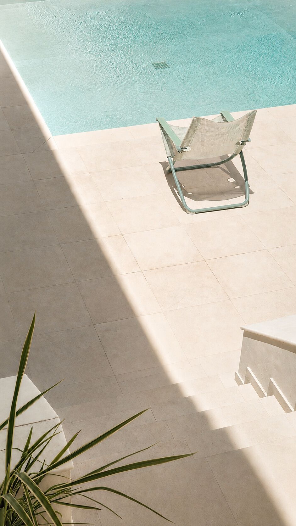 Zona junto a la piscina con una silla, una planta en maceta y una mesa blanca.