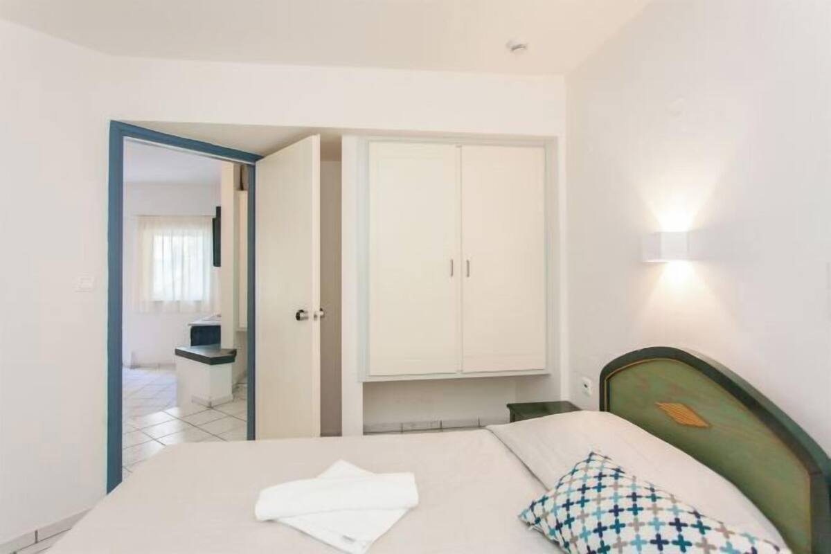 A bedroom with a bed, a wardrobe, a bedside table, and a wall-mounted light.