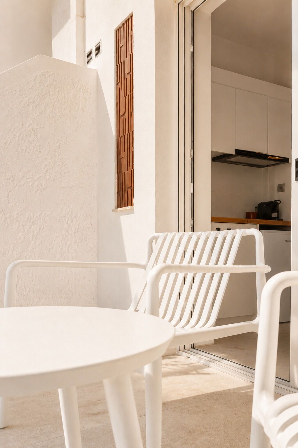 Ein weißer Tisch und Stühle auf einem Balkon, im Hintergrund eine Küche.