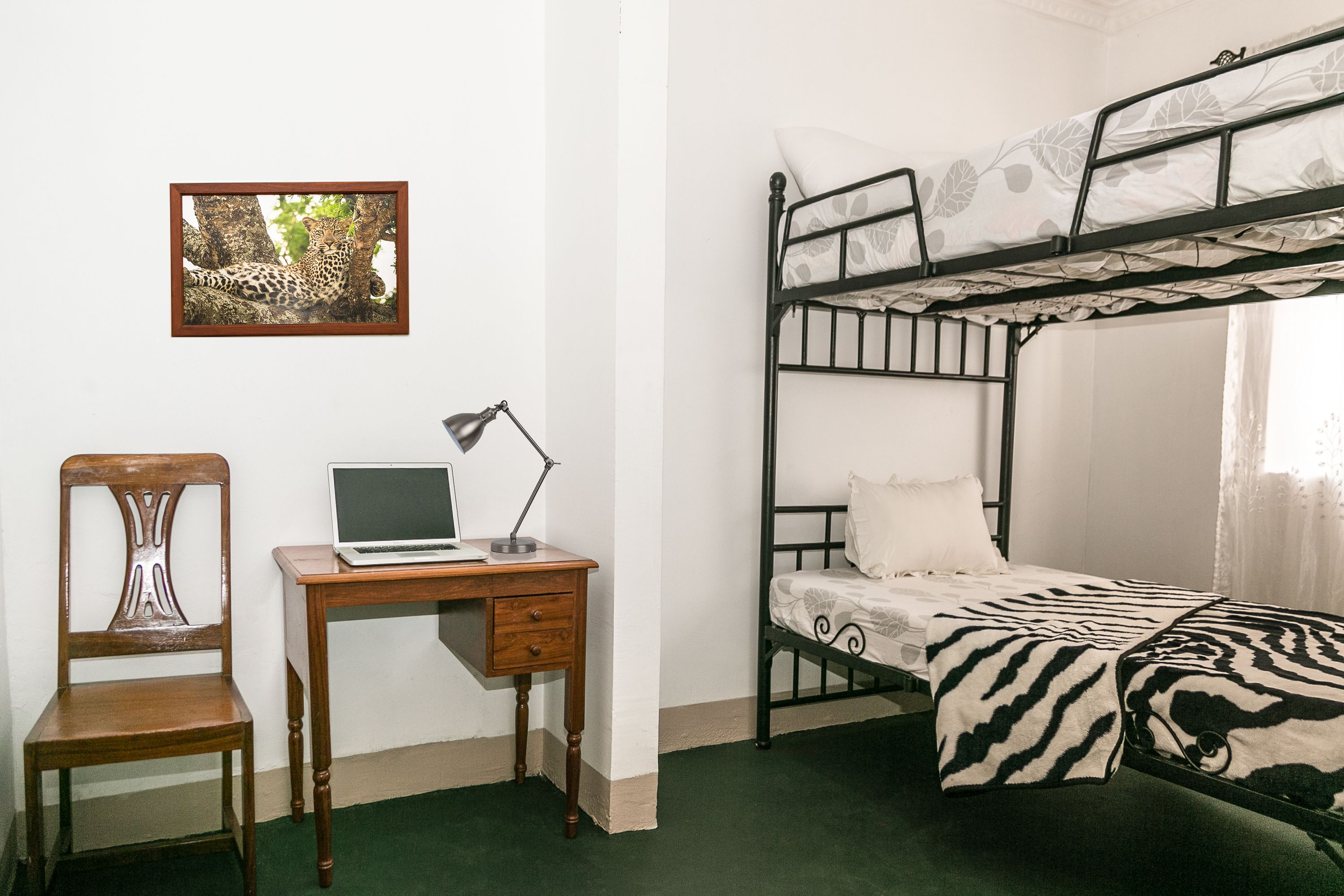 Une chambre avec un lit superposé, un bureau avec un ordinateur portable, une chaise et un tableau encadré au mur.