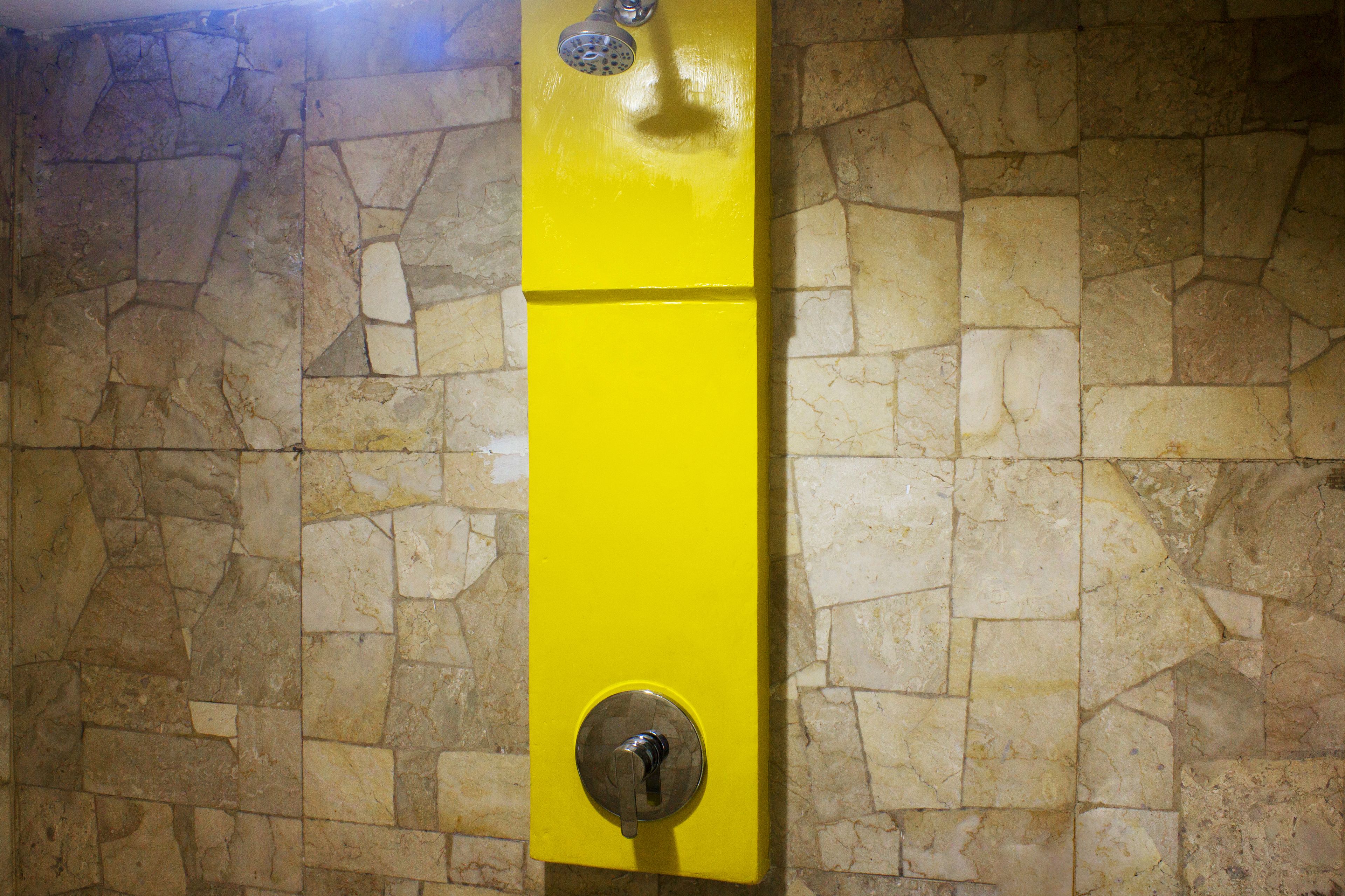 A yellow wall-mounted shower control with a stone wall background.