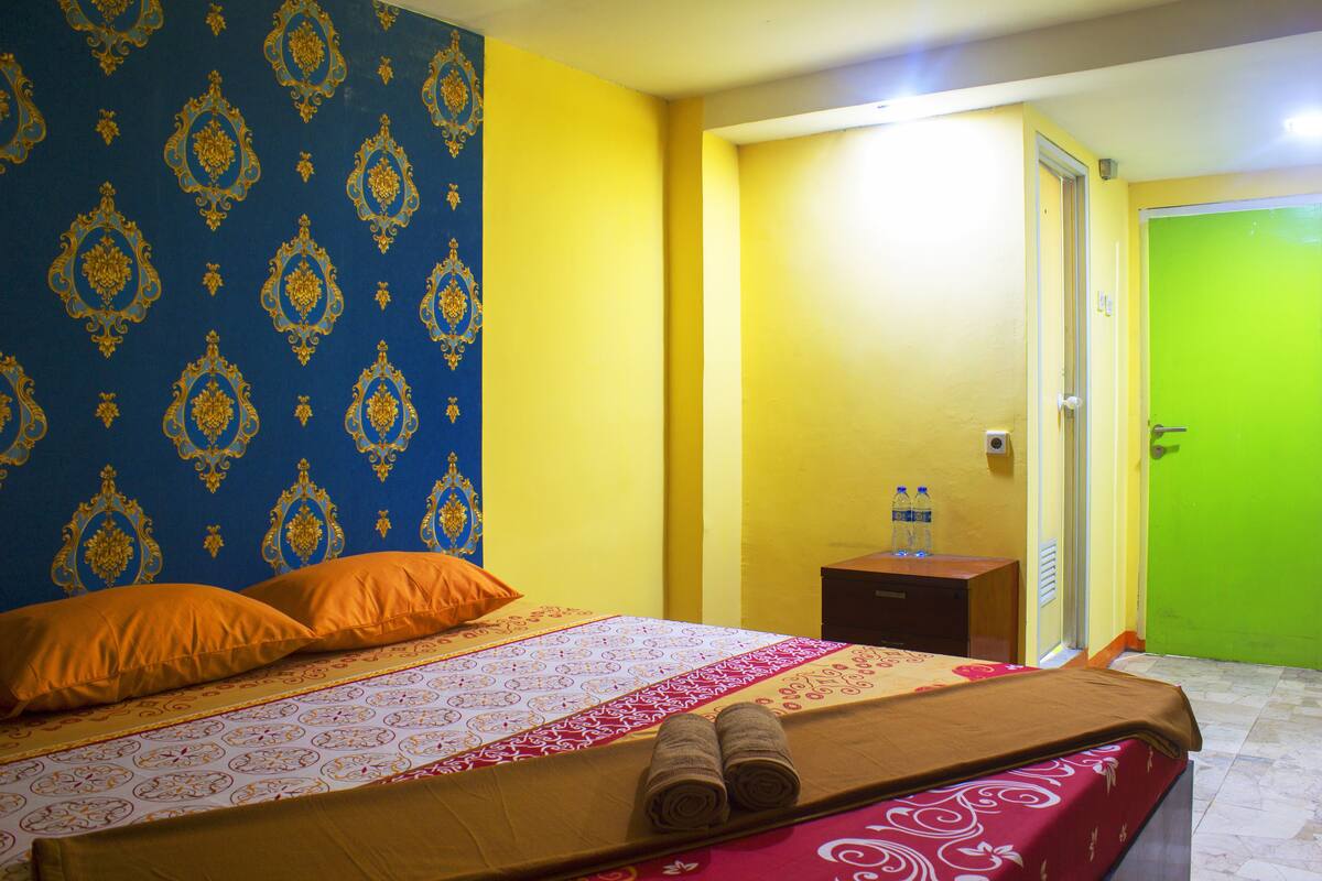 Une chambre d’hôtel avec un lit, deux oreillers, une table de chevet avec des bouteilles d’eau et une porte verte.
