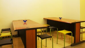 A classroom with two wooden tables, green and black chairs, and a blue decorative object on the tables. - New Priok Indah Hotel (Jakarta)