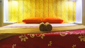 A bed with a red and white floral bedspread, two orange pillows, and rolled towels on the bed. - New Priok Indah Hotel (Jakarta)
