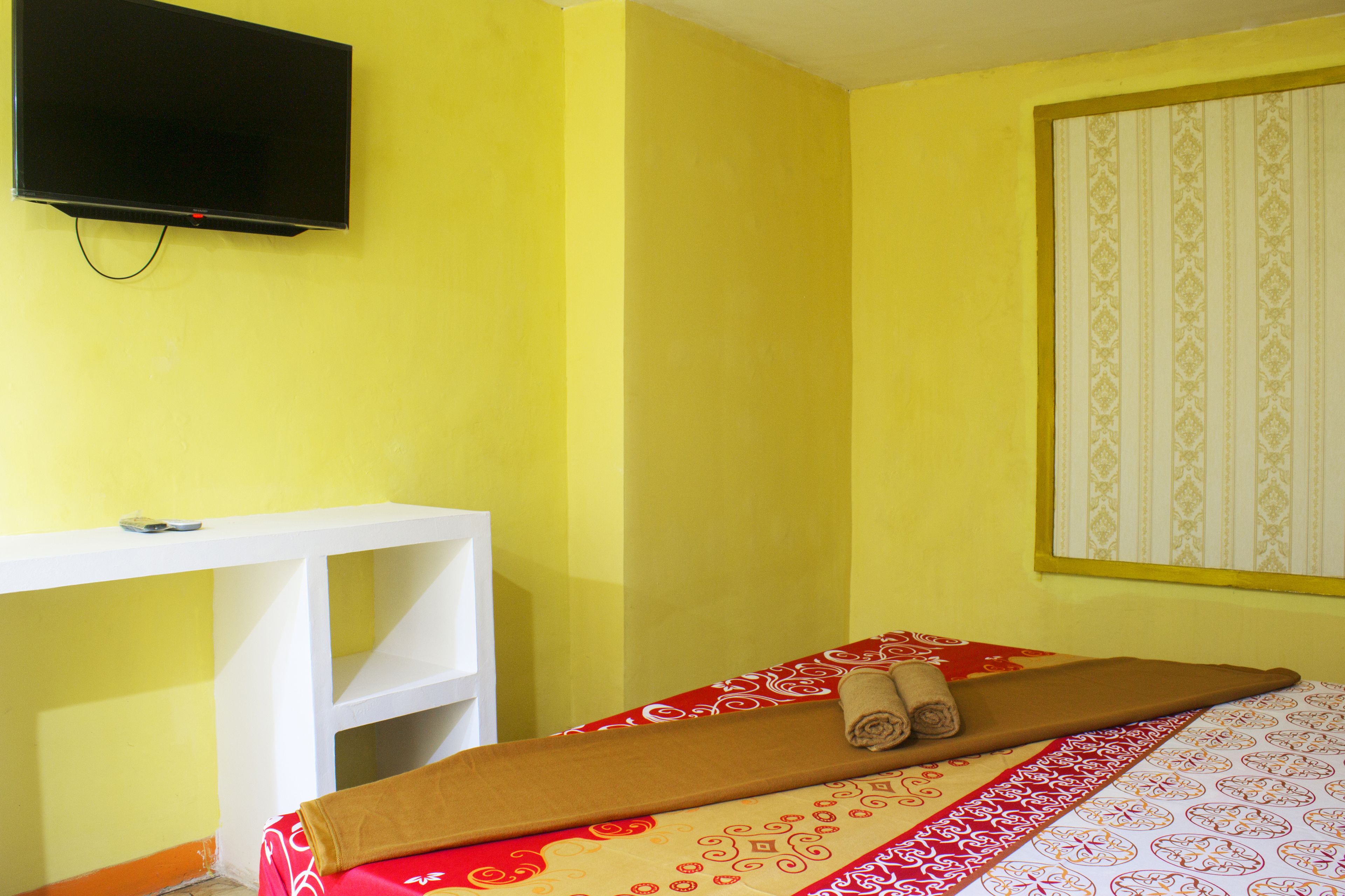 A room with a bed, a desk, a television, and a window with patterned curtains.