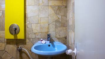 A bathroom with a blue sink, a yellow soap dispenser, and a stone wall.