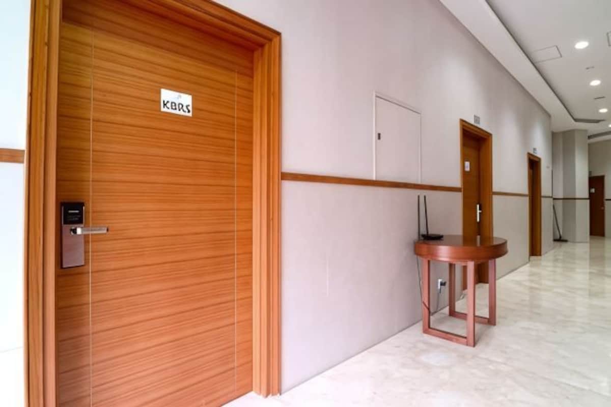 A hallway with wooden doors, a metal door handle, a small table with a chair, and a sign above a door.