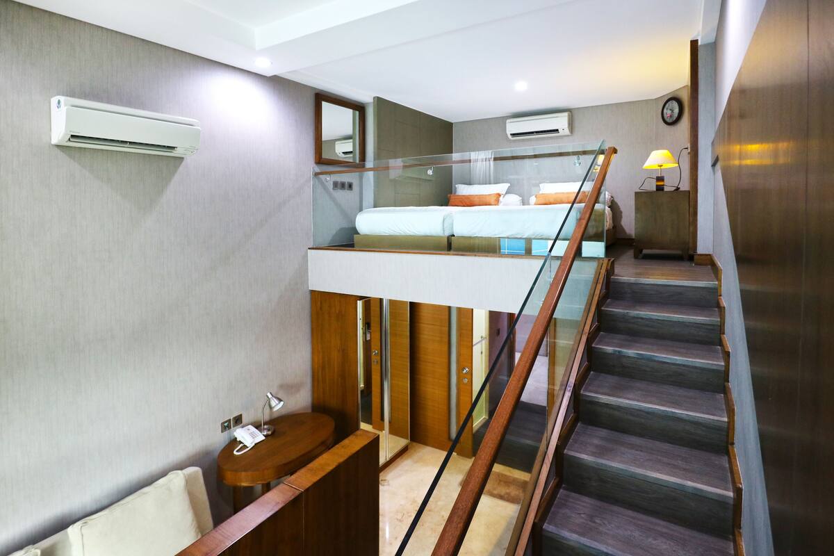 A modern hotel room with a bunk bed, a wooden staircase, and a small bedside table with a lamp.