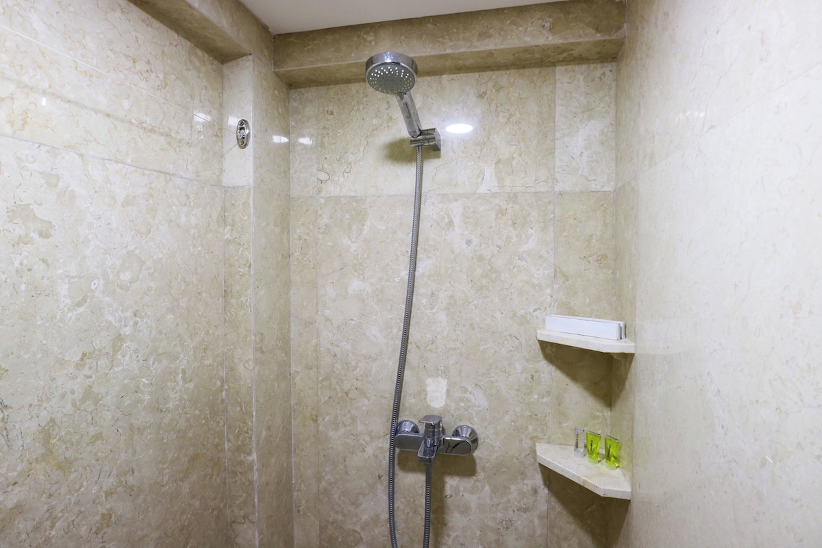A bathroom with a shower, marble walls, and a shelf with toiletries.