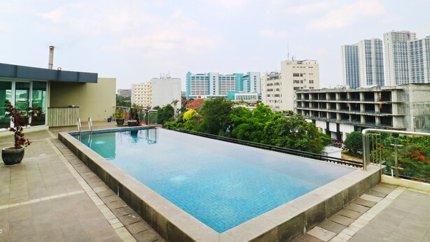 Une piscine sur le toit offrant une vue sur le paysage urbain, entourée de verdure et de bâtiments modernes.