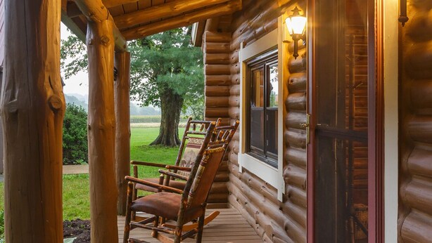 A wooden log cabin with a porch, rocking chairs, and a door with a screen.