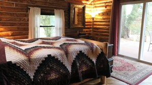 A log cabin bedroom with a large bed, a mirror, and a window with curtains.