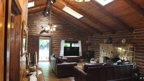 A log cabin interior with a stone fireplace, leather sofas, a television, and a wooden ceiling.
