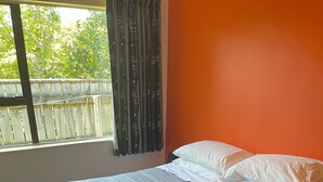 A neatly made bed with striped bedding and pillows, a rolled towel on the bed, and a window with curtains. - Relax in Venice St with four bedrooms and two bathrooms minutes from the square (Martinborough)