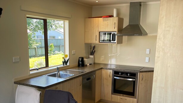 A modern kitchen with a built-in oven, microwave, and stainless steel range hood. There is a window providing natural light and a view of the backyard. - Relax in Venice St with four bedrooms and two bathrooms minutes from the square (Martinborough)