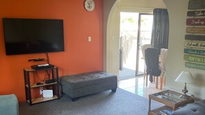 A living room with a flat-screen TV, a grey sofa, a coffee table, and a wall clock. - Relax in Venice St with four bedrooms and two bathrooms minutes from the square (Martinborough)