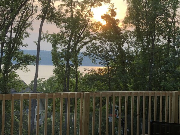 A wooden deck with a basketball hoop, surrounded by trees and a view of a body of water in the background. - Seneca Lake spacious 5-bedroom chalet. Last minute rental discounts available (Hector)