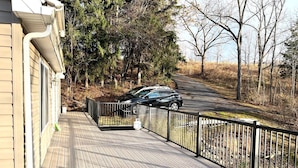 Une terrasse en bois avec une rambarde en métal, une voiture garée dans la rue et des arbres en arrière-plan.