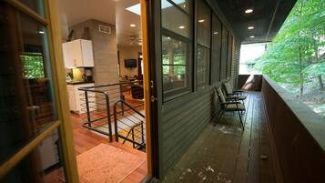 A covered porch with a view of a green landscape, a wooden deck, and a kitchen area with a sink and cabinets.