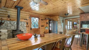 L’intérieur d’un chalet rustique, avec une table à manger en bois, des murs en pierre, une cheminée et un coin cuisine.