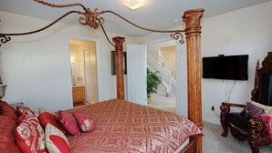 Un dormitorio espacioso con una cama grande, un dosel de madera, un televisor y una escalera que conduce a un piso superior.