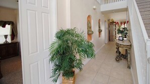 Un pasillo con una puerta blanca, una planta en maceta, una escalera y una mesa decorativa con un florero.