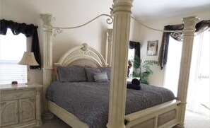 Classic four-poster bed with a textured bedspread and pillows, accompanied by a nightstand and lamp.