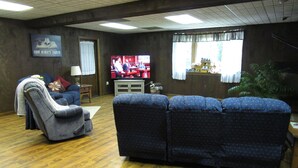 Un salón con un sofá azul, un sillón gris y un televisor mostrando un evento deportivo.
