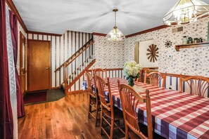 Uma sala de jantar com toalha xadrez, cadeiras de madeira, uma escada e um ornamento floral na parede.