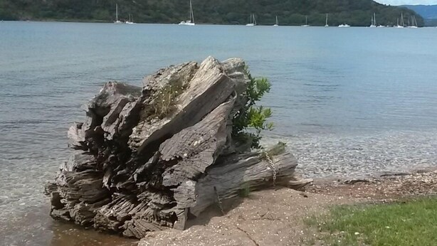 Una gran formación rocosa junto a un lago, con veleros al fondo.