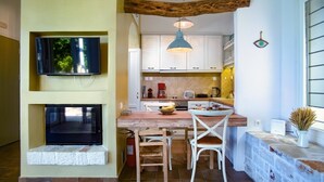 A compact kitchen with a wooden table, white chairs, a hanging light fixture, and a television mounted above the table.