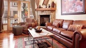 Una sala de estar con sofá de cuero, sillón estampado y chimenea.