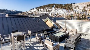 Terraza en la azotea con un área de estar al aire libre de estilo moderno, que incluye sillas y un hogar para fuego, con vistas a un paisaje montañoso nevado.