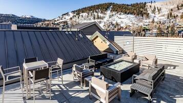 A rooftop terrace with a modern outdoor seating area, including chairs and a fire pit, overlooking a snowy mountain landscape.