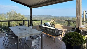 Une terrasse extérieure couverte, aménagée avec une table et des chaises, un canapé et offrant une vue sur la campagne.