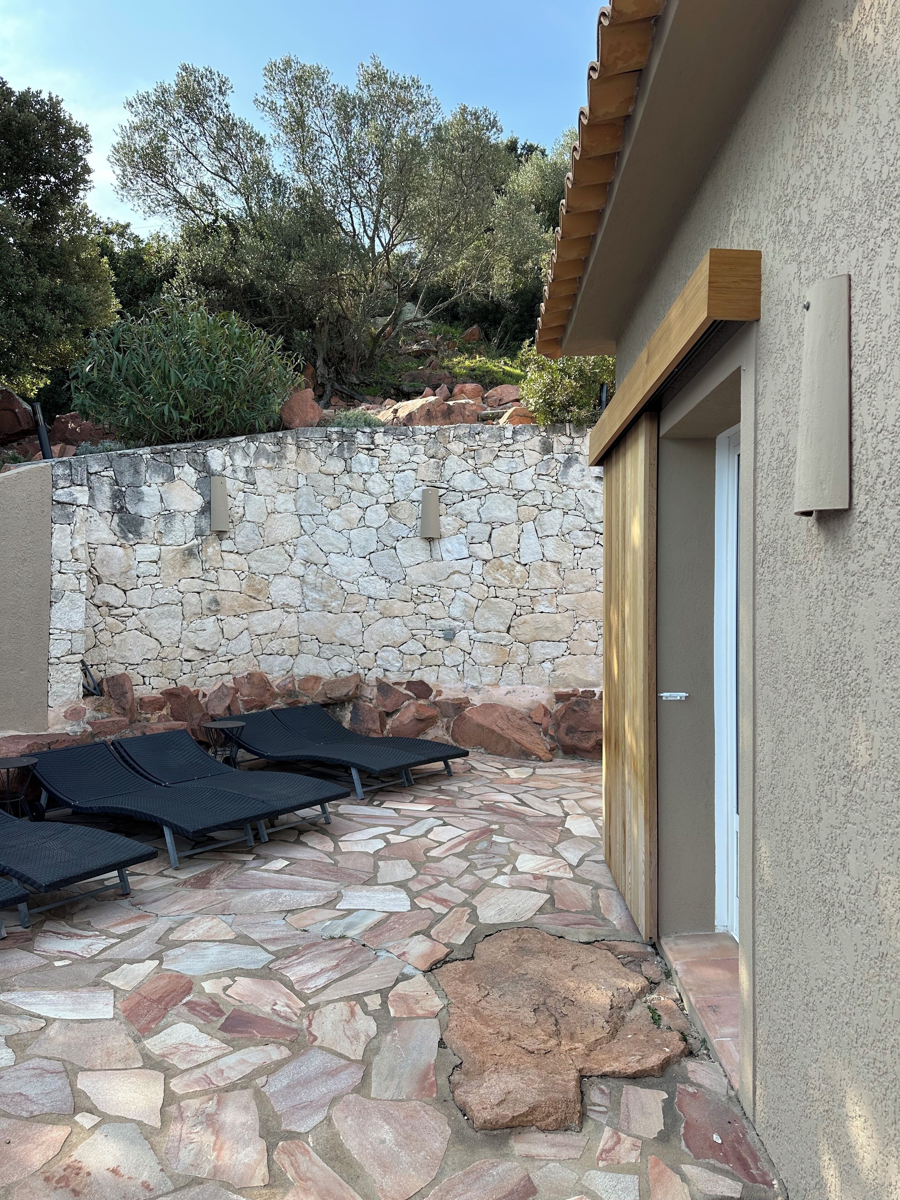 Une terrasse en pierre avec des chaises longues et un mur en pierre.