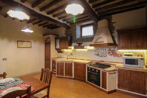 A kitchen with wooden cabinets, a gas stove, a microwave, and hanging utensils. - Wonderful private villa for 20 guests with WIFI, private pool, TV, terrace and pets allowed (Arezzo)