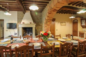 A dining area with a fireplace, wooden beams, and a television mounted on the wall.
