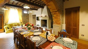 A dining area with a long wooden table set for a meal, flanked by a stone fireplace and a wooden door.