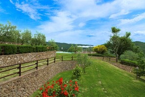 A landscaped garden with a stone wall, a wooden fence, and a view of a lake and hills.