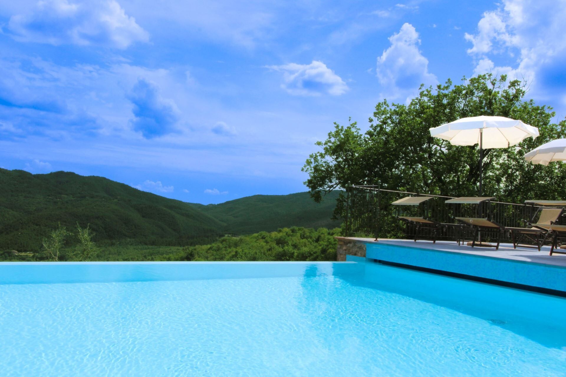 Una piscina azul cristalina con vistas a colinas verdes y un cielo despejado.