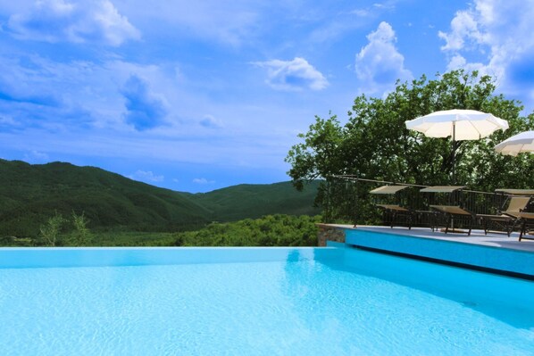 A clear blue swimming pool with a view of green hills and a clear sky.