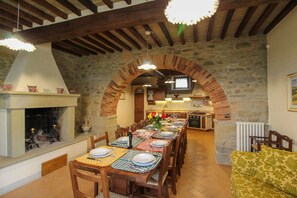 A dining area with a long table set for multiple people, a fireplace, stone walls, and a kitchen in the background. - Wonderful private villa for 20 guests with WIFI, private pool, TV, terrace and pets allowed (Arezzo)