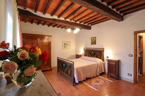 A bedroom with a bed, a nightstand, a wooden ceiling, a painting, and a vase with flowers. - Stunning private villa for 20 guests with private pool, WIFI, TV, terrace and pets allowed (Arezzo)