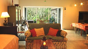 Ein gemütliches Wohnzimmer mit einer Couch, einem Tisch mit einer Kerze und Blick ins Freie durch große Fenster.