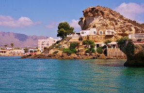 A coastal building with a rocky cliff, multiple balconies, and a view of the sea.
