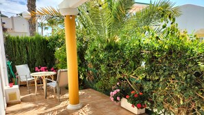 A patio with a yellow column, a table with chairs, and a variety of plants and flowers. - House with terrace of flowers and solarium, near beaches, A/C, wifi, Sat TV, BBQ (San Juan de los Terreros)
